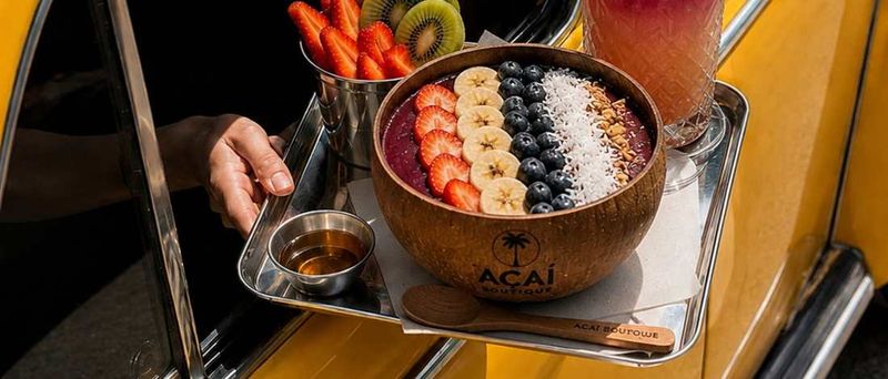 קערת אסאי בקערת קוקוס ממותגת Acai Boutique עם בננה, תות, אוכמניות וקוקוס, מוגשת מהעמדה